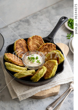 Zucchini fritters or pancakes in fryling pan with fresh herbs and sour cream. Zucchini fritters or pancakes in fryling pan with fresh herbs and sour cream. 96344075