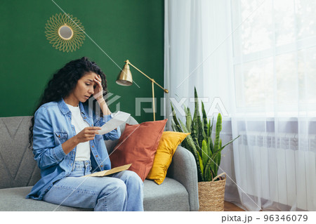 A young Latin American woman received divorce papers. Sitting at home on the rug, holding a sheet of paper in her hands, shocked, holding her head. A young Latin American woman received divorce papers. Sitting at home on the rug, holding a sheet of paper in her hands, shocked, holding her head. 96346079
