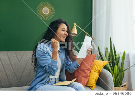 A happy young girl Latin American student received a letter with a notification of successful exams and admission to the university. He is sitting at home on the sofa, holding a letter, reading. A happy young girl Latin American student received a letter with a notification of successful exams and admission to the university. He is sitting at home on the sofa, holding a letter, reading. 96346080