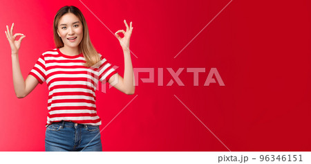 Optimistic good-looking modern asian blond girl show okay fine gesture assure everything ok, smiling broadly, give positive reply, agree good terms, approve excellent effort, red background 96346151