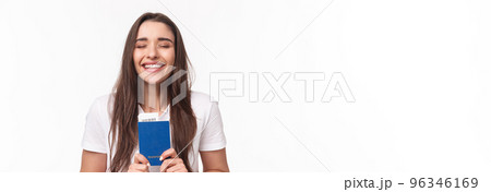 Travelling, holidays, summer concept. Close-up portrait of happy, dreamy girl feeling happy finally travel, holding passport with plane ticket, waiting in airport, standing white background Travelling, holidays, summer concept. Close-up portrait of happy, dreamy girl feeling happy finally travel, holding passport with plane ticket, waiting in airport, standing white background 96346169