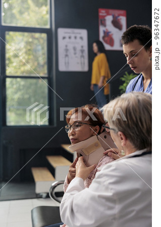 Medical staff helping senior woman to take off neck collar, trying to recovery after accident injury. Injured patient with cervical foam brace receiving help from doctor and nurse in health center. 96347672
