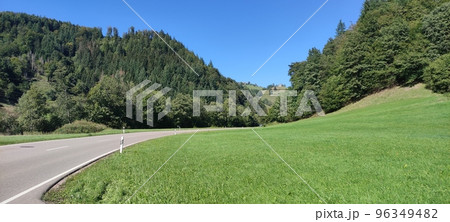 A beautiful view of a gray road crossing hills that are covered with trees passing near green grass under us a blue sky suitable for a background for a desktop A beautiful view of a gray road crossing hills that are covered with trees passing near green grass under us a blue sky suitable for a background for a desktop 96349482