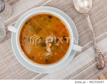 Pickle soup with pearl barley, potatoes, onions, carrots and parsley. Rassolnik in a white plate on a marble background. Traditional dish of Russian cuisine Pickle soup with pearl barley, potatoes, onions, carrots and parsley. Rassolnik in a white plate on a marble background. Traditional dish of Russian cuisine 96350087