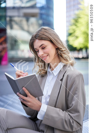A young woman in corporate suit, sits with notebook and pen, takes notes, works and writes down her ideas 96350509