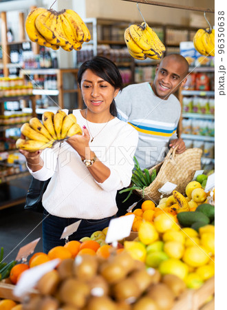 Hispanic married couple choosing bananas in grocery store 96350638