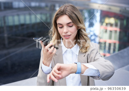 Businesswoman checks time on digital watch and records voice message, arranges a meeting, sits outside in city centre 96350639