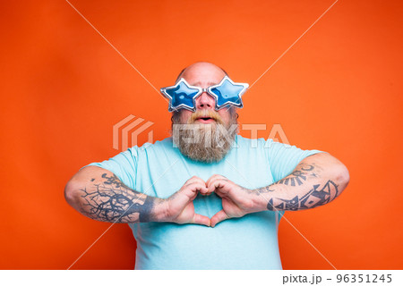 Fat man with beard, tattoos and sunglasses makes heart shape with hands 96351245