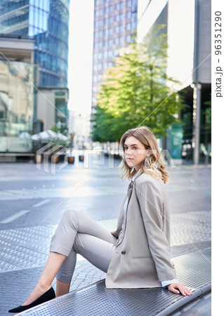 Vertical shot of successful young lady in suit, sitting outdoors, waiting for someone outside office. Employee relaxing on fresh air Vertical shot of successful young lady in suit, sitting outdoors, waiting for someone outside office. Employee relaxing on fresh air 96351290