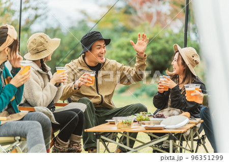秋冬のキャンプ場で仲間と一緒にビールを飲みながら冗談を言って盛り上げる人気者のアジア人男性 96351299