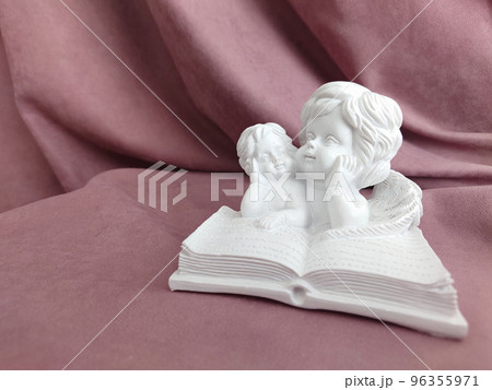 Reading a big book, a white figurine of angels in close-up Reading a big book, a white figurine of angels in close-up 96355971