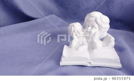 Figurines of little angels reading a book on a lilac background Figurines of little angels reading a book on a lilac background 96355975
