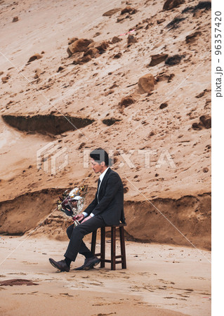砂浜で椅子にブーケを持って座る男性 96357420