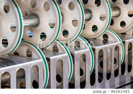 Part of an industrial machine tool in a factory . A lot of round plastic wheels for pulling the sleeve for cutting bags. 96362485