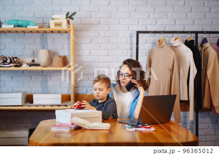 Young mother works with little boy. Business Woman talking on the phone and discussing work issues. 96365012