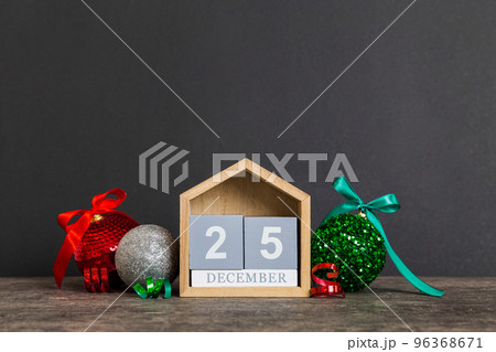25 december. Christmas composition on colored background with a wooden calendar, with a gift box, toys, bauble copy space 25 december. Christmas composition on colored background with a wooden calendar, with a gift box, toys, bauble copy space 96368671