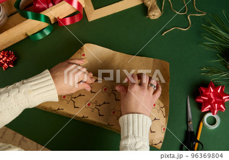 Top view of woman's hands wrapping a present for Christmas or New Year's events over green background. Boxing Day 96369804