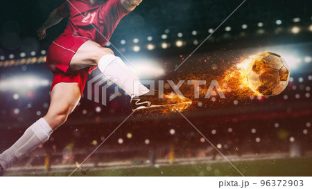Close up of a soccer scene at night match with player in a red uniform kicking a fiery ball with power 96372903