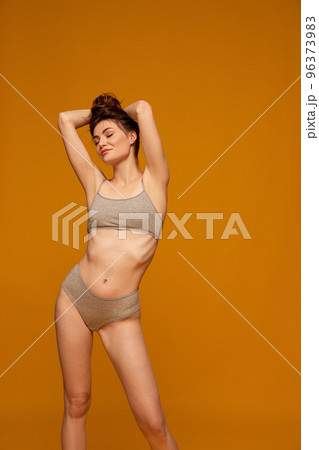 Portrait of young beautiful woman posing in grey underwear isolated over yellow studio background. Taking care after body shape Portrait of young beautiful woman posing in grey underwear isolated over yellow studio background. Taking care after body shape 96373983