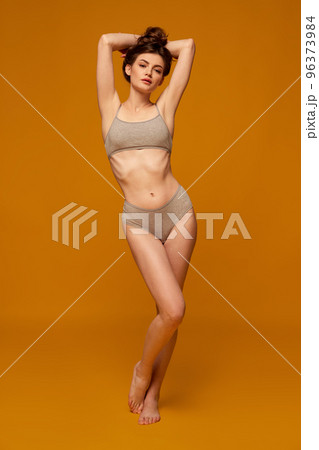 Portrait of young beautiful woman posing in grey underwear isolated over yellow studio background. Slim body shape 96373984