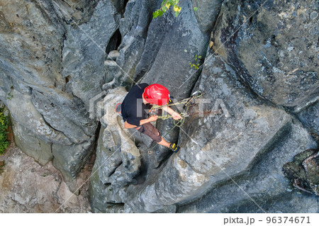 Young man climbing steep wall of rocky mountain. Male climber overcomes challenging route. Engaging in extreme sport concept. 96374671
