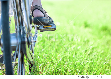 Womans foot on bicycle pedal on green grass closeup 96374698
