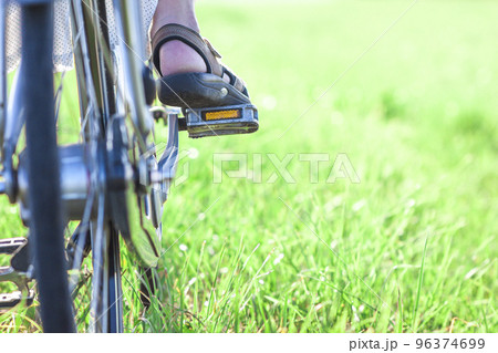 Womans foot on bicycle pedal on green grass closeup 96374699