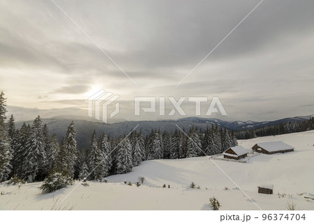 Winter mountain landscape. Old wooden houses on snowy clearing on background of mountain ridge, spruce forest and cloudy sky. Happy New Year and Merry Christmas card. Winter mountain landscape. Old wooden houses on snowy clearing on background of mountain ridge, spruce forest and cloudy sky. Happy New Year and Merry Christmas card. 96374704