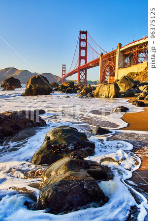 Waves crash around rocks on beach next to Golden Gate Bridge in San Francisco near sunset 96375125