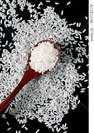 White raw rice in wooden spoons on black background. Natural organic vegan food. Uncooked grains of long rice are scattered ontable. Traditional Asian cereal culture. Vertical photo. 96378228