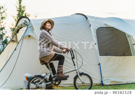 愛犬と秋冬のキャンプ場で自転車に乗ってサイクリングするアジア人女性 96382528
