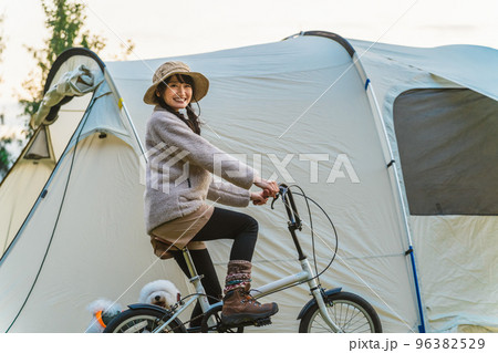 愛犬と秋冬のキャンプ場で自転車に乗ってサイクリングするアジア人女性 96382529