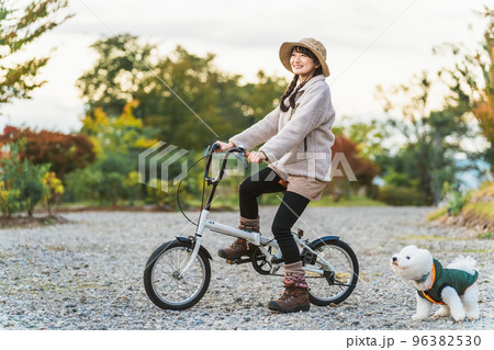 愛犬と秋冬のキャンプ場で自転車に乗ってサイクリングするアジア人女性 96382530
