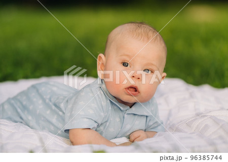 Cute happy toddler lying on a blanket on the grass outdoors in summer Cute happy toddler lying on a blanket on the grass outdoors in summer 96385744