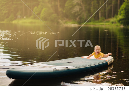 The child lies floating on the water on a large sup board. Water sports 96385753