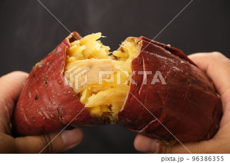 さつまいもの焼き芋を手で半分に割って湯気が出ている 96386355