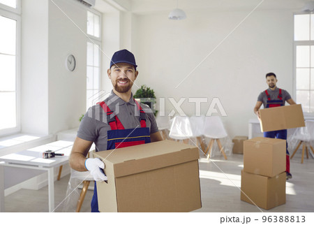 Portrait of smiling male loader with colleague taking cardboard boxes out of client's house. Portrait of smiling male loader with colleague taking cardboard boxes out of client's house. 96388813