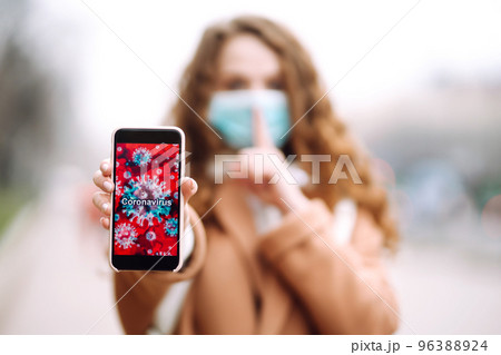 Girl in protective sterile medical mask on her face holds out the phone in quarantine city. 96388924