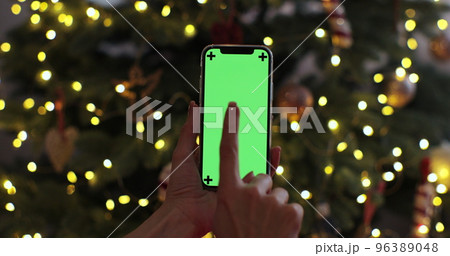 Closeup woman hand is holding chroma key green screen touching on christmas background. Using phone with green mock-up, surfing internet. Closeup woman hand is holding chroma key green screen touching on christmas background. Using phone with green mock-up, surfing internet. 96389048