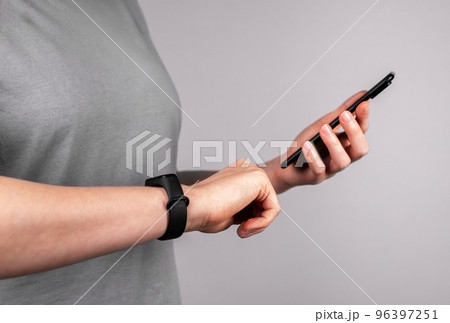 Woman with fitness bracelet at wrist using mobile app at phone for checking physical activity results or connecting watches to smartphone. Healthy lifestyle concept 96397251