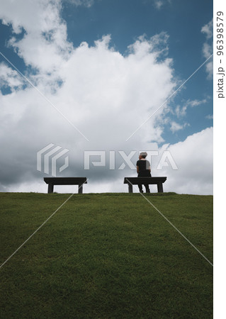 Rear view point ofyoung woman relaxing on a park bench ,with green grass ,blue sky and cloud Rear view point ofyoung woman relaxing on a park bench ,with green grass ,blue sky and cloud 96398579