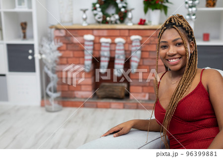 Smiling African woman sits on a sofa in a red dress. Christmas decoration. 96399881