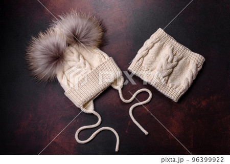 Beautiful white knitted winter cap with pompons on a dark concrete background Beautiful white knitted winter cap with pompons on a dark concrete background 96399922
