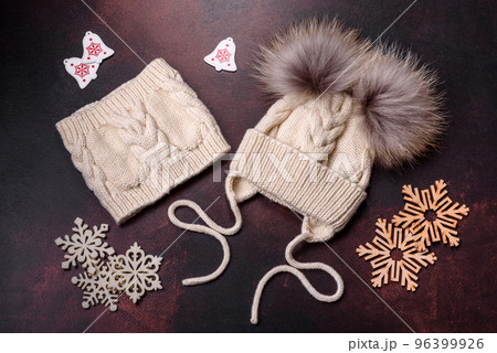 Beautiful white knitted winter cap with pompons on a dark concrete background Beautiful white knitted winter cap with pompons on a dark concrete background 96399926