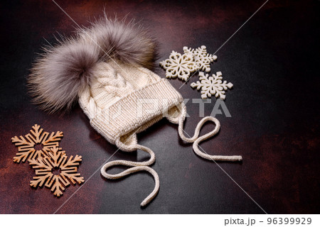 Beautiful white knitted winter cap with pompons on a dark concrete background 96399929