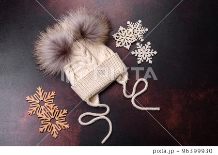 Beautiful white knitted winter cap with pompons on a dark concrete background Beautiful white knitted winter cap with pompons on a dark concrete background 96399930