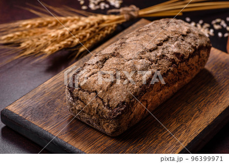 A loaf of brown bread with grains of cereals on a wooden cutting board A loaf of brown bread with grains of cereals on a wooden cutting board 96399971