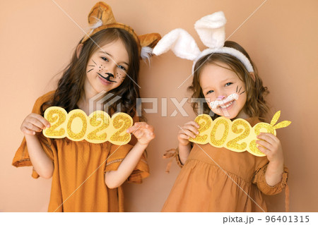 Funny girls show the numbers 2022 and 2023 of the new year. Children dressed up in animals with tiger and rabbit painted on their faces Funny girls show the numbers 2022 and 2023 of the new year. Children dressed up in animals with tiger and rabbit painted on their faces 96401315