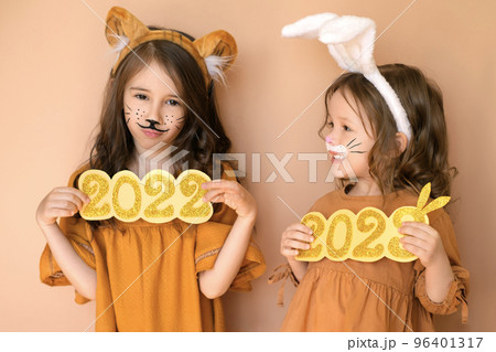 A sad girl with the number 2022 in the guise of a tiger and a child with the number 2023 new year dressed up as a bunny. A sad girl with the number 2022 in the guise of a tiger and a child with the number 2023 new year dressed up as a bunny. 96401317