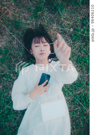 寝そべってスマホとイヤホン持つ若い女性の写真 寝そべってスマホとイヤホン持つ若い女性の写真 96406210